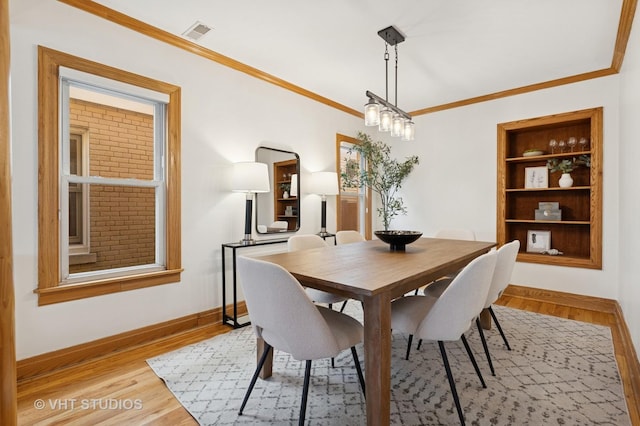 dining room featuring visible vents, light wood-style flooring, built in shelves, and ornamental molding