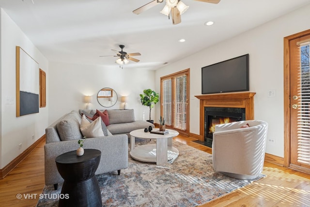 living area with wood finished floors, baseboards, a fireplace with flush hearth, recessed lighting, and ceiling fan