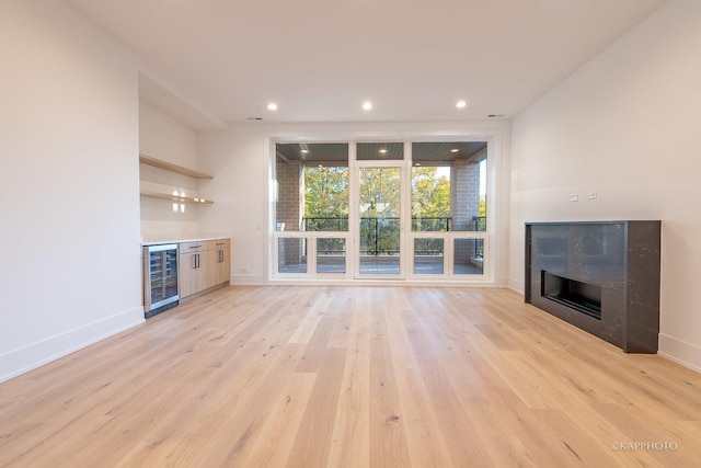 unfurnished living room featuring a dry bar, light wood-style flooring, a tile fireplace, beverage cooler, and baseboards