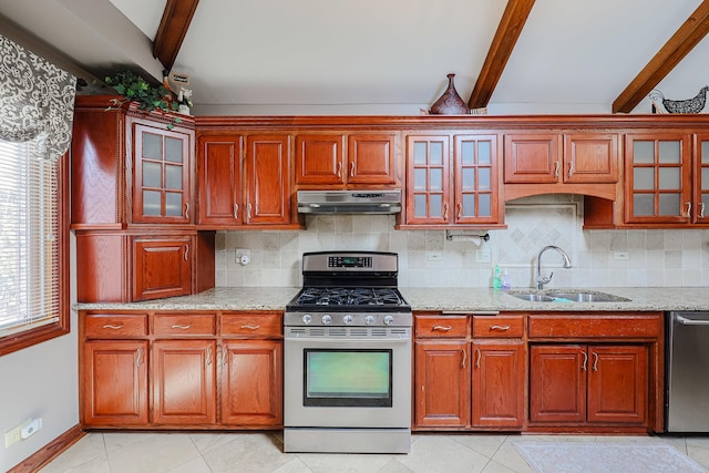 kitchen featuring under cabinet range hood, light stone counters, a sink, stainless steel appliances, and decorative backsplash