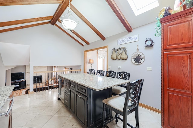 kitchen featuring light stone counters, a kitchen island, beam ceiling, a skylight, and a kitchen bar