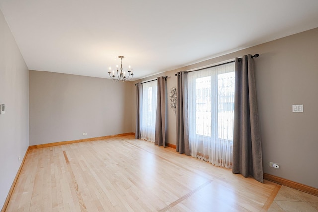 empty room featuring baseboards, an inviting chandelier, and light wood finished floors