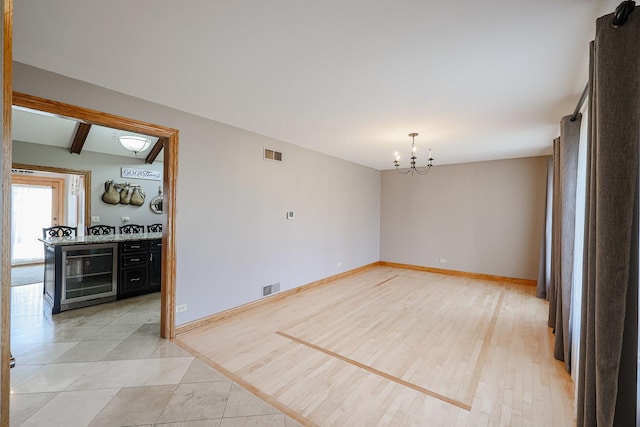 spare room featuring wine cooler, baseboards, visible vents, and light wood-type flooring