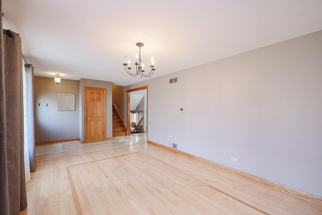 spare room featuring light wood finished floors, visible vents, baseboards, stairs, and a notable chandelier