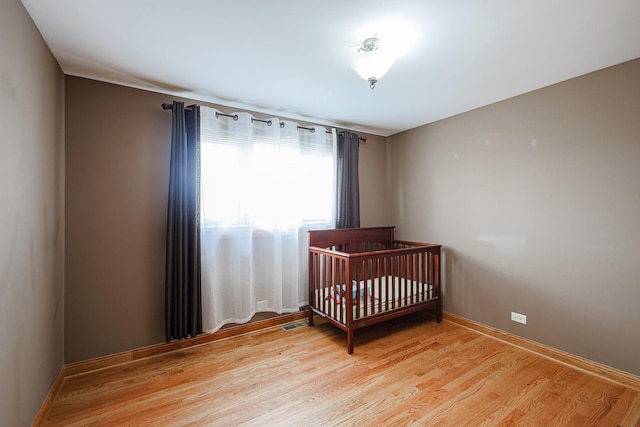 bedroom with visible vents, a crib, baseboards, and light wood-style floors