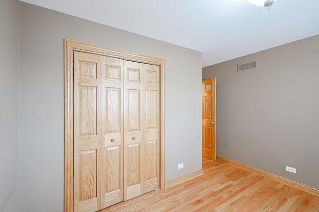 unfurnished bedroom featuring light wood-style floors, visible vents, a closet, and baseboards