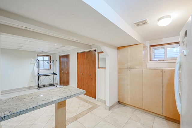 basement with arched walkways, visible vents, baseboards, and light tile patterned floors