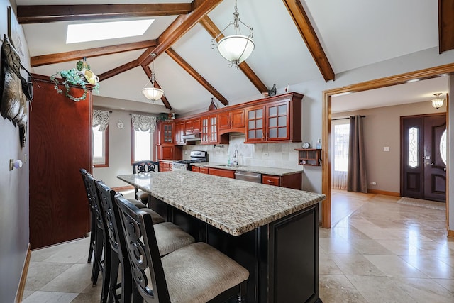 kitchen featuring backsplash, light stone countertops, lofted ceiling with beams, stainless steel appliances, and a sink