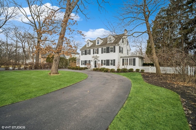 view of front facade featuring aphalt driveway, a front yard, fence, and a chimney