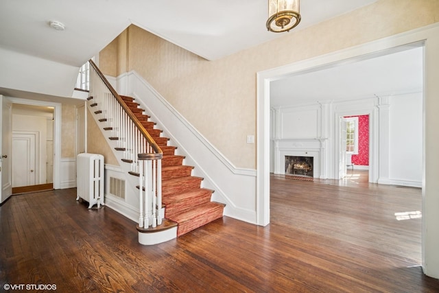 stairway featuring a decorative wall, a fireplace, wood finished floors, and radiator