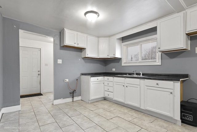 kitchen featuring dark countertops, a sink, white cabinetry, and baseboards