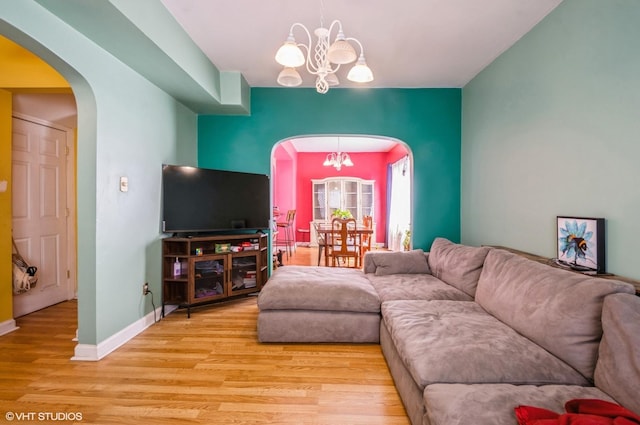 living area featuring an inviting chandelier, baseboards, arched walkways, and wood finished floors