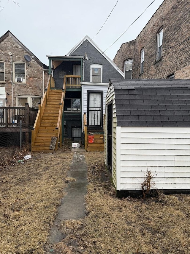 rear view of house featuring an outbuilding, a storage shed, roof with shingles, and a deck