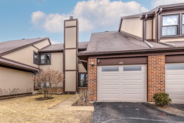 view of front of house featuring aphalt driveway, brick siding, a chimney, and a garage