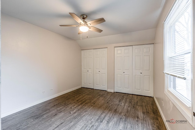 unfurnished bedroom featuring baseboards, a ceiling fan, lofted ceiling, dark wood-style flooring, and two closets