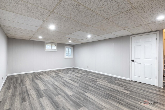 basement featuring a drop ceiling, wood finished floors, and baseboards