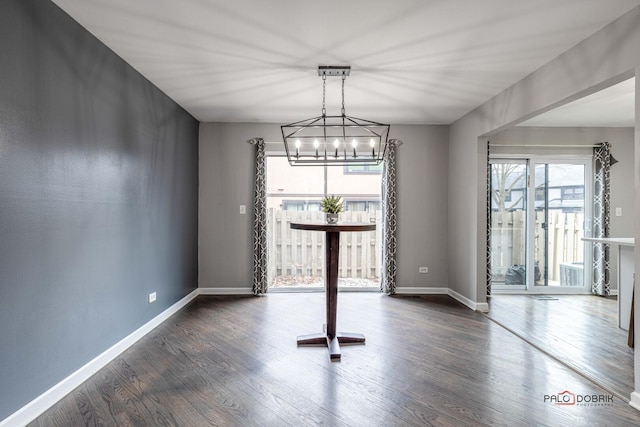 unfurnished dining area with dark wood-type flooring, baseboards, and an inviting chandelier