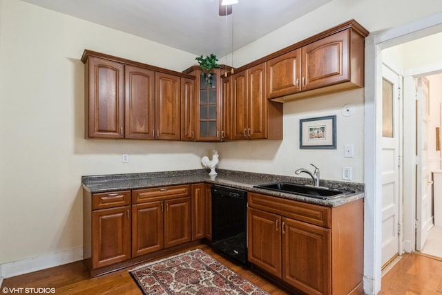 kitchen with dishwasher, dark countertops, glass insert cabinets, wood finished floors, and a sink