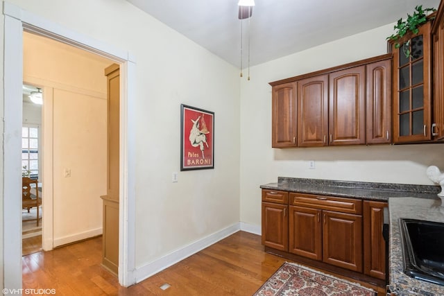 kitchen with glass insert cabinets, ceiling fan, baseboards, and wood finished floors