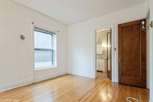 unfurnished bedroom with connected bathroom, light wood-style flooring, and baseboards