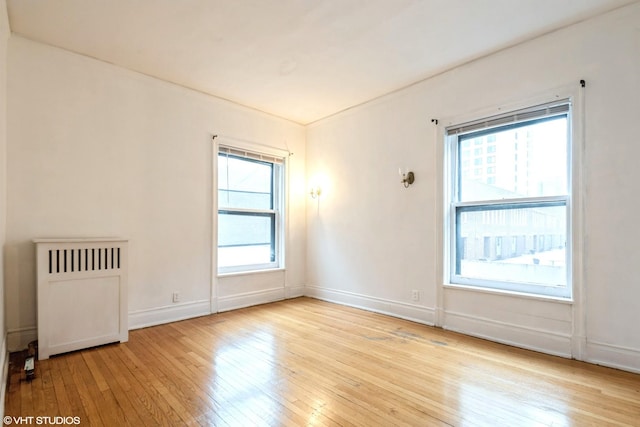 unfurnished room featuring radiator heating unit, light wood-type flooring, and baseboards