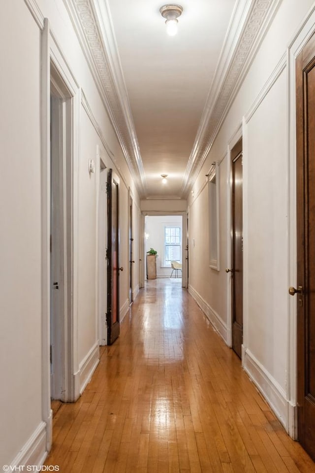 hall featuring light wood-style floors, baseboards, and ornamental molding