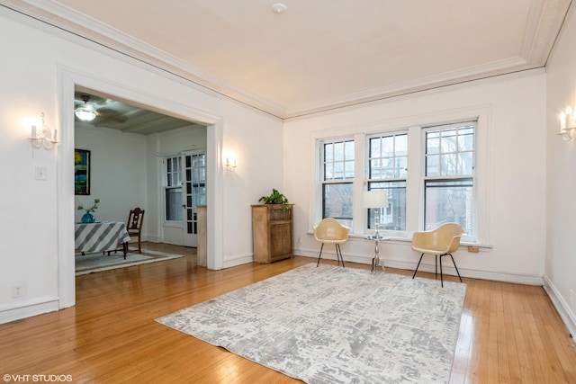 living area with ornamental molding, light wood-style floors, and baseboards