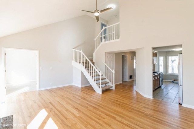 unfurnished living room featuring light wood-style floors, stairway, baseboards, and a ceiling fan