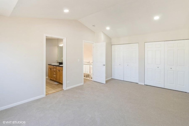 unfurnished bedroom with ensuite bathroom, light colored carpet, baseboards, vaulted ceiling, and two closets