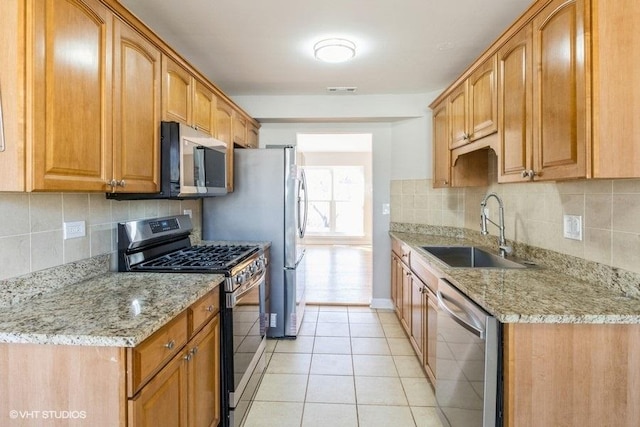 kitchen with stainless steel appliances, light tile patterned flooring, a sink, and light stone countertops