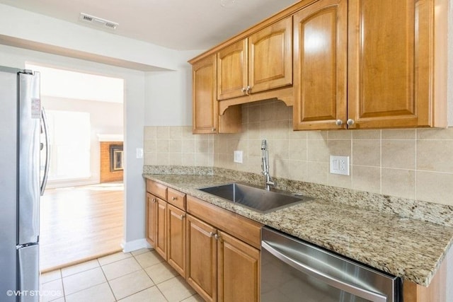 kitchen featuring light stone counters, stainless steel appliances, a sink, visible vents, and backsplash