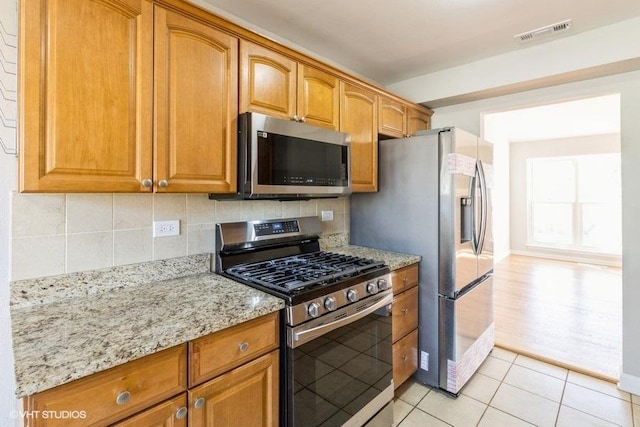 kitchen with stainless steel appliances, light stone counters, backsplash, and visible vents