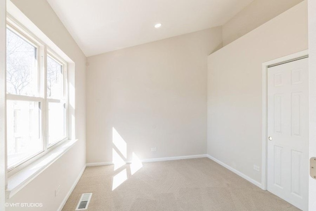 empty room featuring visible vents, baseboards, vaulted ceiling, and light colored carpet