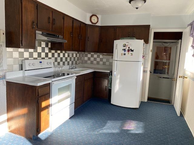 kitchen featuring dark brown cabinets, under cabinet range hood, light countertops, white appliances, and a sink