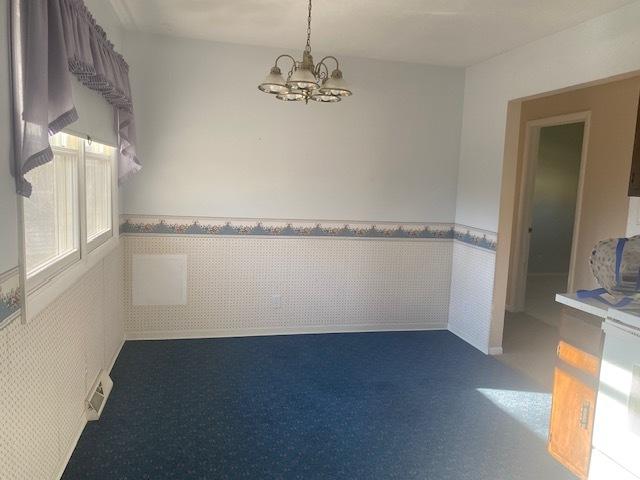 spare room with a wainscoted wall, tile walls, and an inviting chandelier