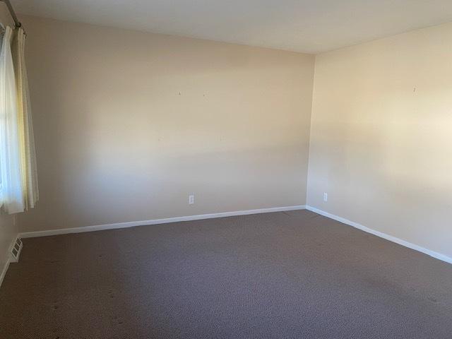 empty room with visible vents, baseboards, and dark carpet