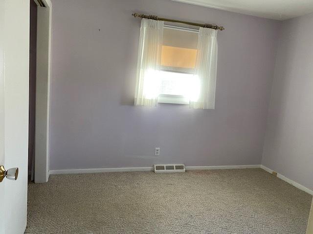 carpeted spare room with visible vents and baseboards