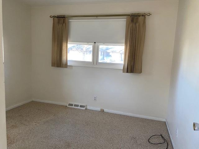 carpeted spare room featuring visible vents and baseboards