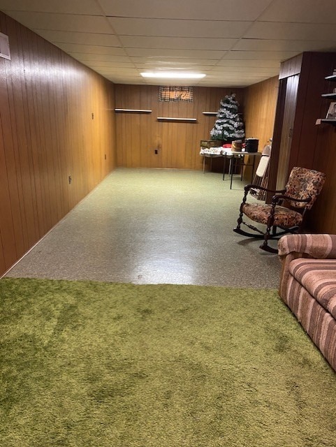 interior space featuring a drop ceiling, wood walls, and carpet flooring