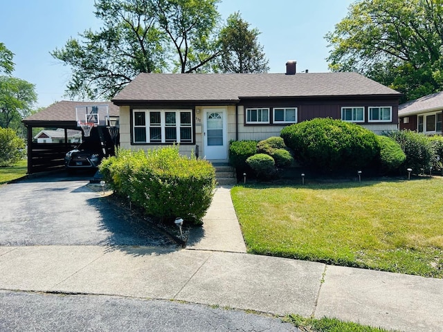 ranch-style home with a chimney, a shingled roof, an attached carport, driveway, and a front lawn