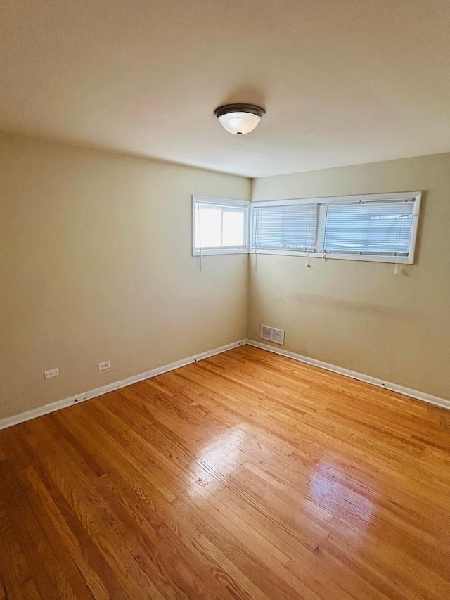 spare room with light wood-type flooring, visible vents, and baseboards