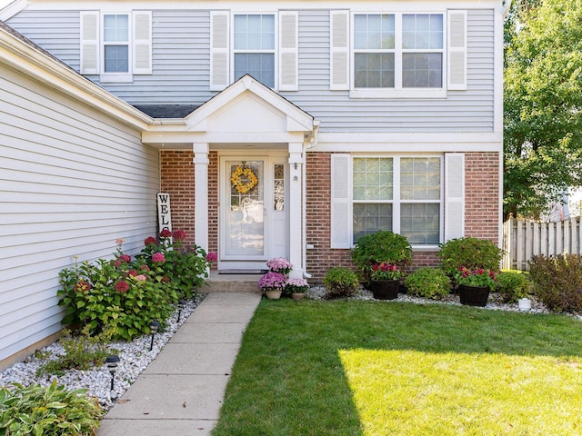 doorway to property featuring brick siding, a lawn, and fence