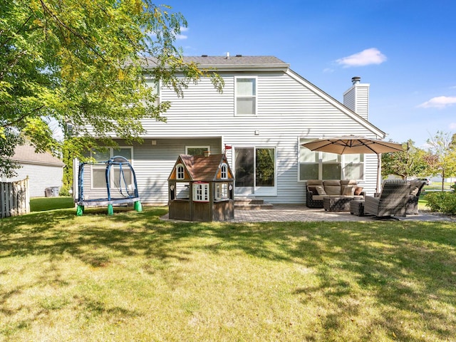 back of house featuring a yard, a trampoline, a chimney, and a patio area