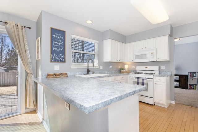 kitchen featuring a sink, white appliances, a peninsula, white cabinets, and light countertops