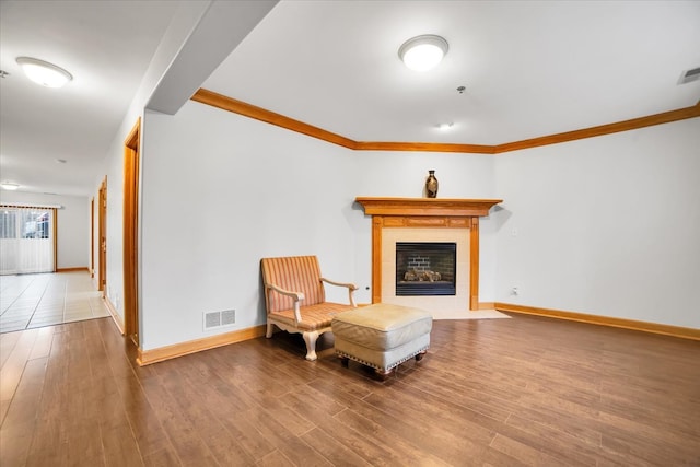 living area with baseboards, visible vents, a tiled fireplace, wood finished floors, and crown molding