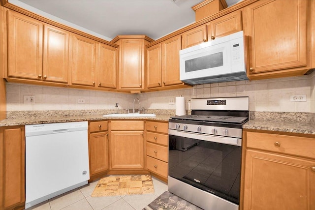 kitchen featuring white appliances, light tile patterned floors, decorative backsplash, light stone countertops, and a sink