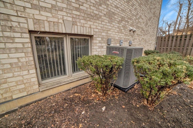 exterior details featuring central AC unit, fence, and brick siding