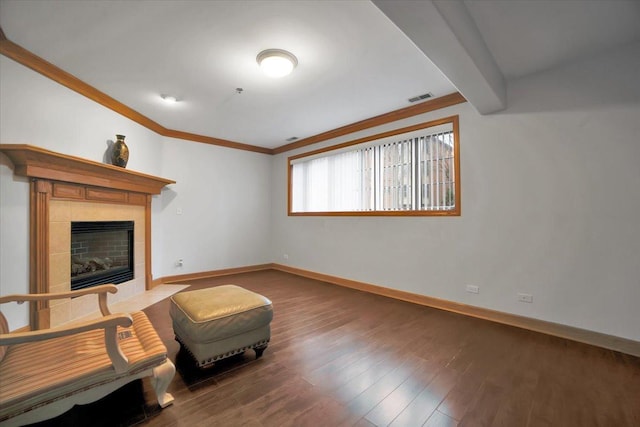 sitting room featuring visible vents, baseboards, a tile fireplace, wood finished floors, and crown molding