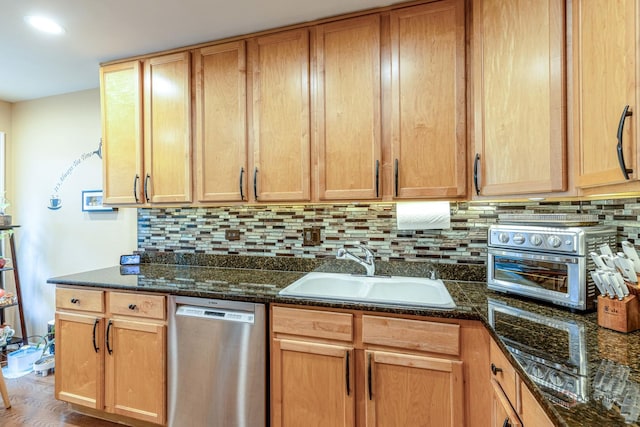 kitchen featuring dark stone countertops, a toaster, a sink, stainless steel dishwasher, and tasteful backsplash