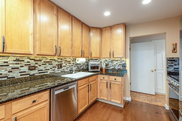 kitchen with a sink, dark stone countertops, tasteful backsplash, stove, and dishwasher